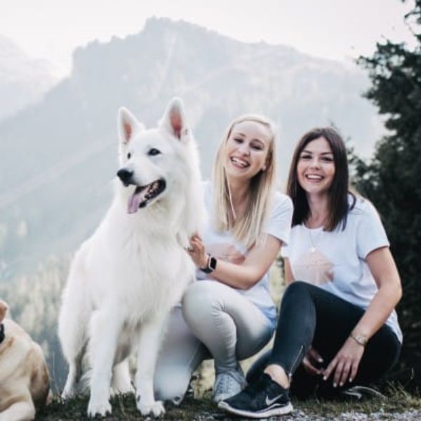 Zwei Frauen sitzen lachend mit einem Hund vor Bergen vom Ratgeber Unsere Pawsitive Life Coaches von Liebesgut Tiernahrung